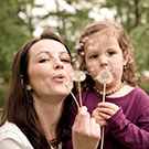 woman and girl blowing on dandelion blossom