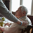 woman comforting elderly man sitting at a table