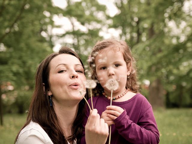 woman and child blowing on dandelion blossom