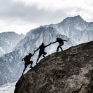 Three fellow mountain climbers helping one another ascend.