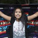 Native American girl smiling and holding up tribal blanket